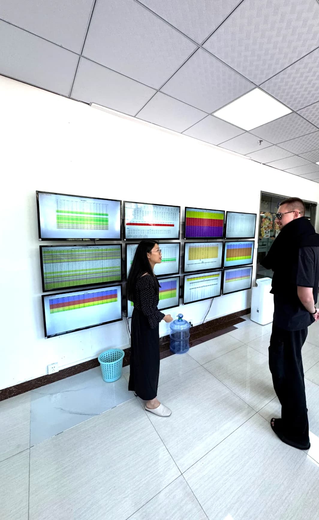 Two people reviewing a wall of monitors showing live data dashboards in the studio.